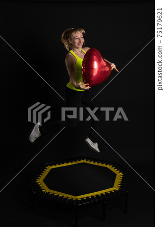 Girl on a fitness trampoline on a black background in a yellow t-shirt yellow energy sport, active activity athlete girl movement, club. Fly motion, sportswear muscle instructor enjoy 75179621
