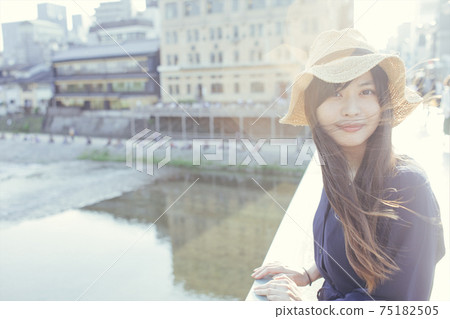 A woman with long hair looking at the camera wearing a straw hat on a bridge in Kyoto A woman with long hair looking at the camera wearing a straw hat on a bridge in Kyoto 75182505