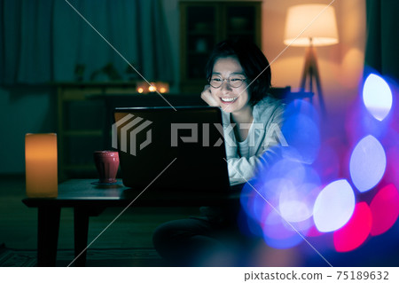 A smiling young woman looking at a computer in the living room at night A smiling young woman looking at a computer in the living room at night 75189632