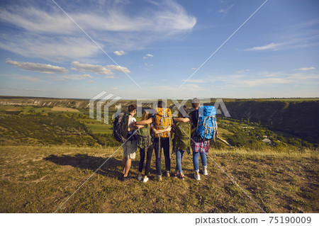 Group of hikers with backpacks standing on mountain top and observing scenery, back view. Young friends on camping trip Group of hikers with backpacks standing on mountain top and observing scenery, back view. Young friends on camping trip 75190009
