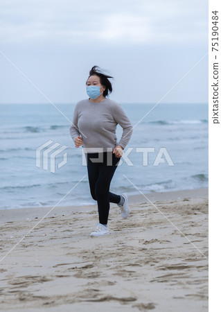 Asian woman with a mask running on the beach 75190484