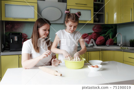 Young mother and daughter together prepare dough in the kitchen Young mother and daughter together prepare dough in the kitchen 75198019