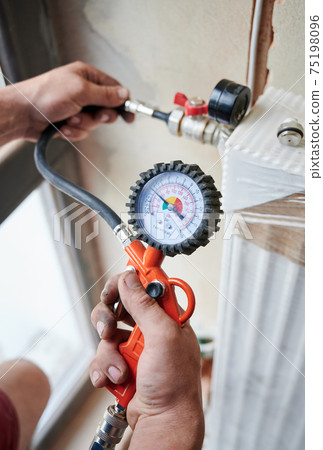Hands of a plumber holding pressure sensors of water supply 75198096