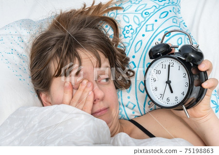 Woman with alarm clock does not want waking up at early 75198863