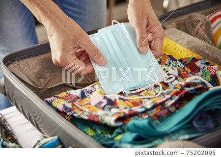 man packing face masks in his holidays suitcase 75202095
