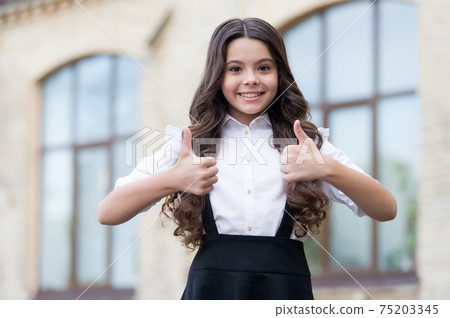 Happy kid show thumbs ups wearing uniform with back to school look outdoors, approval 75203345
