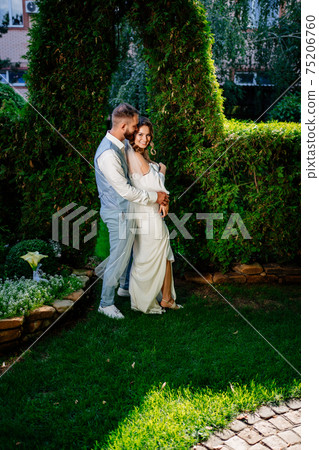Happy and beautiful bride and groom gently cuddle in the park 75206760