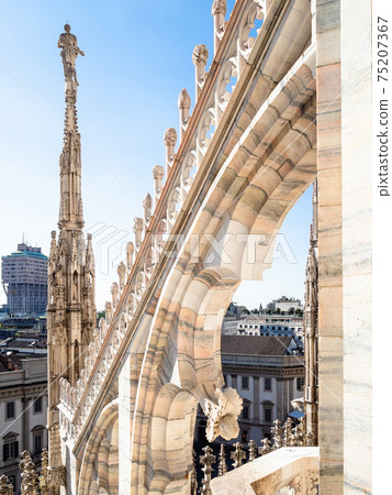 statue on spire of Duomo di Milano roof over city 75207367