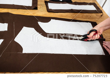 female hand cuts brown fabric by scissors 75207723