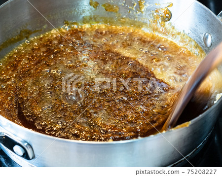 cooking salted butter caramel sauce at home kitchen - stirring boiled mixture of sugar and butter with wooden culinary spatula in steel pan 75208227