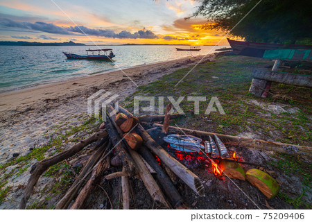 Fish bbq on tropical desert beach. Cooking barbecue with wood fire at sunset, colorful sky on sea, dramatic clouds, getting away, adventure in Indonesia Sumatra Banyak Islands 75209406