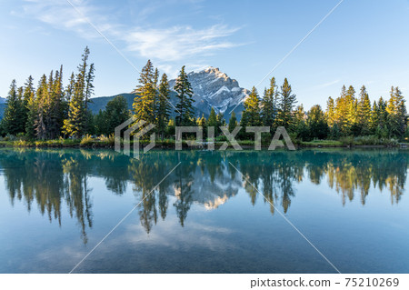 Banff National Park beautiful scenery. Cascade Mountain and pine trees reflected on turquoise color Bow River in summer time. Town of Banff, Canadian Rockies, Alberta, Canada. Banff National Park beautiful scenery. Cascade Mountain and pine trees reflected on turquoise color Bow River in summer time. Town of Banff, Canadian Rockies, Alberta, Canada. 75210269
