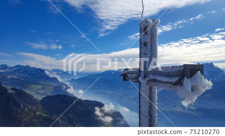 Icy summit cross on the top of Federispitz, a Swiss mountain. View to Walensee. Icy summit cross on the top of Federispitz, a Swiss mountain. View to Walensee. 75210270