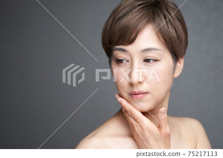 A middle-aged Japanese woman who diverts her eyes and puts her hand on her cheek 75217113