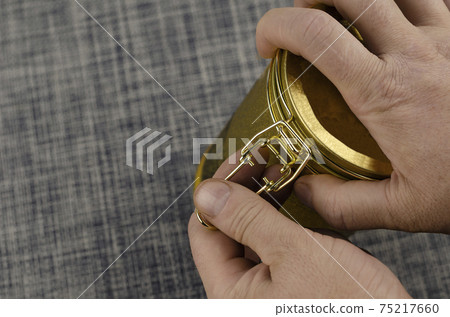 Man's hand opens Tea coffee tin with clasp close-up. Gold latch lock tin for dry goods. Selective focus. Man's hand opens Tea coffee tin with clasp close-up. Gold latch lock tin for dry goods. Selective focus. 75217660