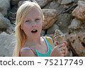 Young blonde girl surprised and holding a seashell 75217749