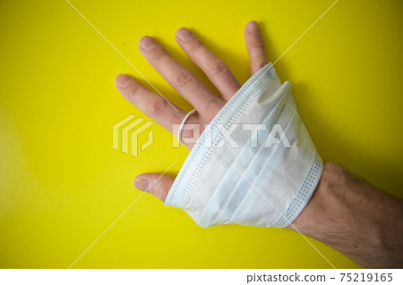A protective medical mask is wrapped around the arm. Background of yellow artistic oil paint. Mask in hand 75219165