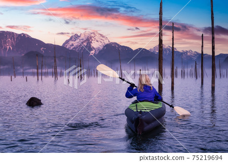 Adventurous Girl kayaking on an infatable kayak in a beautiful lake Adventurous Girl kayaking on an infatable kayak in a beautiful lake 75219694