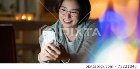 年輕女子看著她的智能手機在客廳裡在晚上橫幅大小 75221846