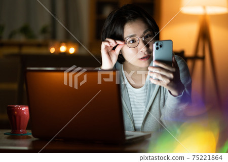 A young woman looking at her smartphone in the living room at night A young woman looking at her smartphone in the living room at night 75221864