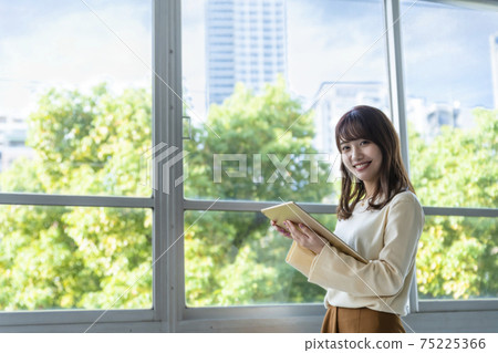 A woman holding a tablet and standing by the window A woman holding a tablet and standing by the window 75225366