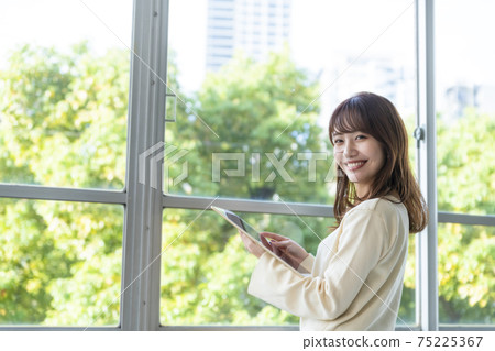 A woman holding a tablet and standing by the window A woman holding a tablet and standing by the window 75225367