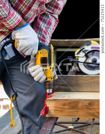 Man drilling a hole in the wooden board. Man drilling a hole in the wooden board. 75225413