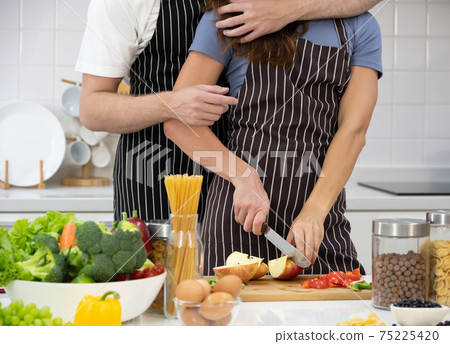 Young couple cutting apple fruit in the kitchen, girl hugging her guy. Healthy Dieting Food Concept. . Young couple cutting apple fruit in the kitchen, girl hugging her guy. Healthy Dieting Food Concept. . 75225420