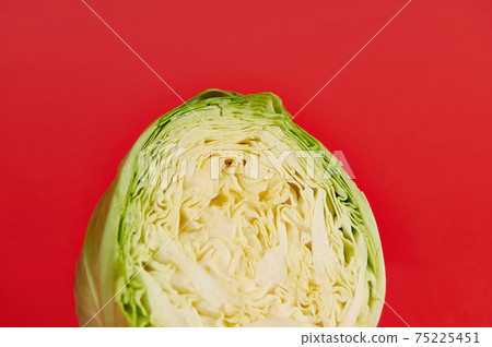 Cropped image of a half cut young green cabbage on a red background with copy space. Color contrast. Cropped image of a half cut young green cabbage on a red background with copy space. Color contrast. 75225451