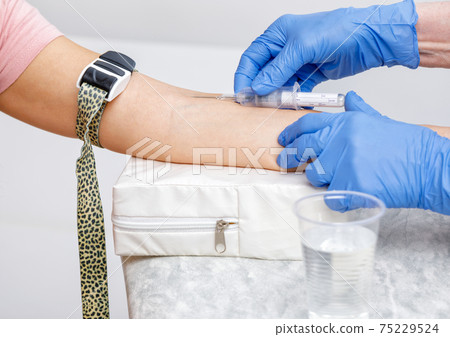 Nurse takes a blood sample from arm vein performing a venipuncture Nurse takes a blood sample from arm vein performing a venipuncture 75229524
