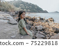 little girl sitting on rock over sea 75229818