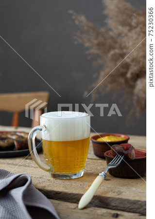 Glass with beer and foam and fork with a piece of sausage Glass with beer and foam and fork with a piece of sausage 75230366