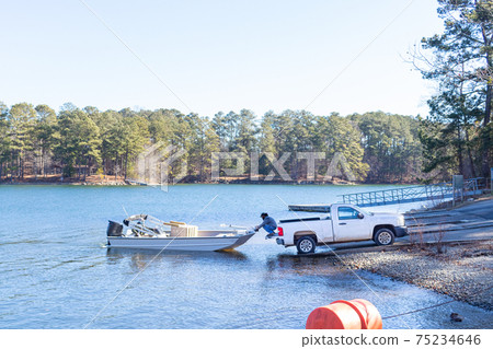 Pickup truck pulling boat and trailer out of the water at the shore of a lake.. 75234646