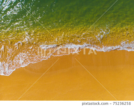 Top view of a deserted coast of golden sand and turquoise green clear sea with waves and foam. Aerial view Top view of a deserted coast of golden sand and turquoise green clear sea with waves and foam. Aerial view 75236258