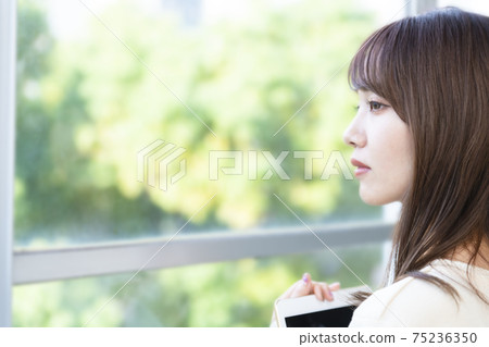 A woman holding a tablet and standing by the window 75236350