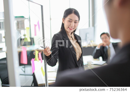 asia business man and woman pointing to paper post it on glass board explain document with manager in the office.businesswoman in meeting with colleagues, gesturing.Selective Focus asia business man and woman pointing to paper post it on glass board explain document with manager in the office.businesswoman in meeting with colleagues, gesturing.Selective Focus 75236364