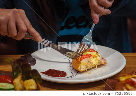 Female hands holding fork and knife to cut a slice of pizza on white plate, selective focus 75236595