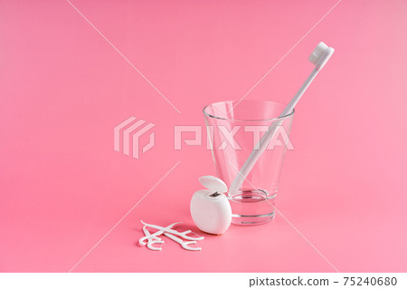 Fashionable toothbrush with soft bristles. Popular toothbrushes. Hygiene trends. Oral hygiene kit. Toothbrushes in glass, floss thread and toothpicks on a pink background 75240680