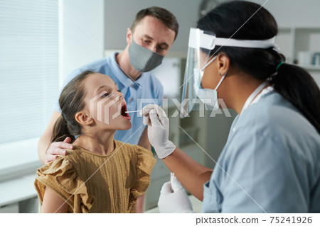 Little girl sitting in front of nurse testing her for covid with cotton bud Little girl sitting in front of nurse testing her for covid with cotton bud 75241926