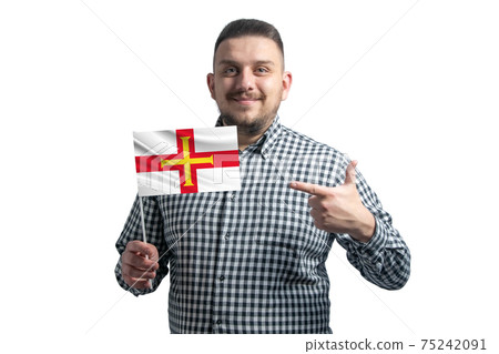 White guy holding a flag of Guernsey and points the finger of the other hand at the flag isolated on a white background 75242091