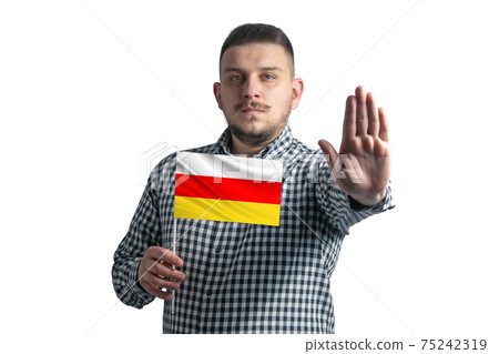 White guy holding a flag of South Ossetia and with a serious face shows a hand stop sign isolated on a white background White guy holding a flag of South Ossetia and with a serious face shows a hand stop sign isolated on a white background 75242319