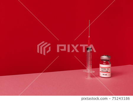 Medical bottle with covid 19 vaccine and syringe on red backdrop with tilted trendy skyline and copy space. 75243186