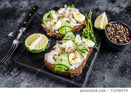 Fresh toasts with shrimp, prawns, quail eggs and cucumber on rye bread. Black background. top view Fresh toasts with shrimp, prawns, quail eggs and cucumber on rye bread. Black background. top view 75246074