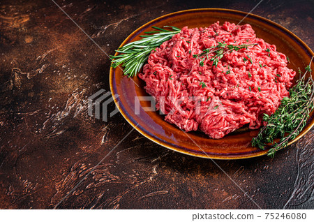 Raw ground beef or veal meat on a rustic plate with herbs. Dark background. Top view. Copy space 75246080