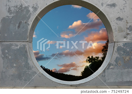 View of white clouds in sunset sky through hole in concrete wall View of white clouds in sunset sky through hole in concrete wall 75249724