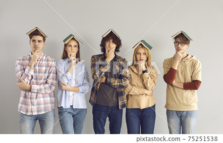 Students stand on a gray background with a pensive expression having books on their heads. 75251538