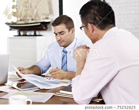 asian and caucasian business executives reviewing and discussing business performance in office 75252025