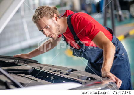 Serious repairman looking under hood of car 75257378