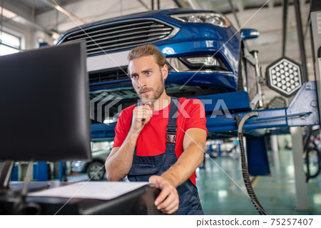 Involved repairman looking at computer in garage Involved repairman looking at computer in garage 75257407