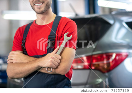 Smiling auto mechanic with wrench near a car Smiling auto mechanic with wrench near a car 75257529